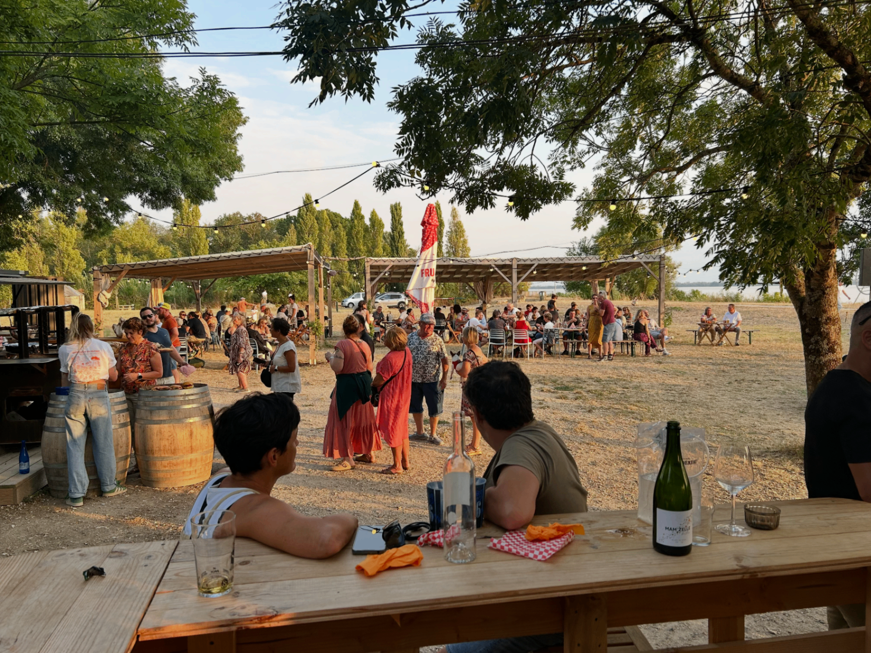 Ambiance conviviale en fin de journée à la Guinguette du Peyrat, guirlandes lumineuses et public rassemblé. - réalisé par Agence Kulte